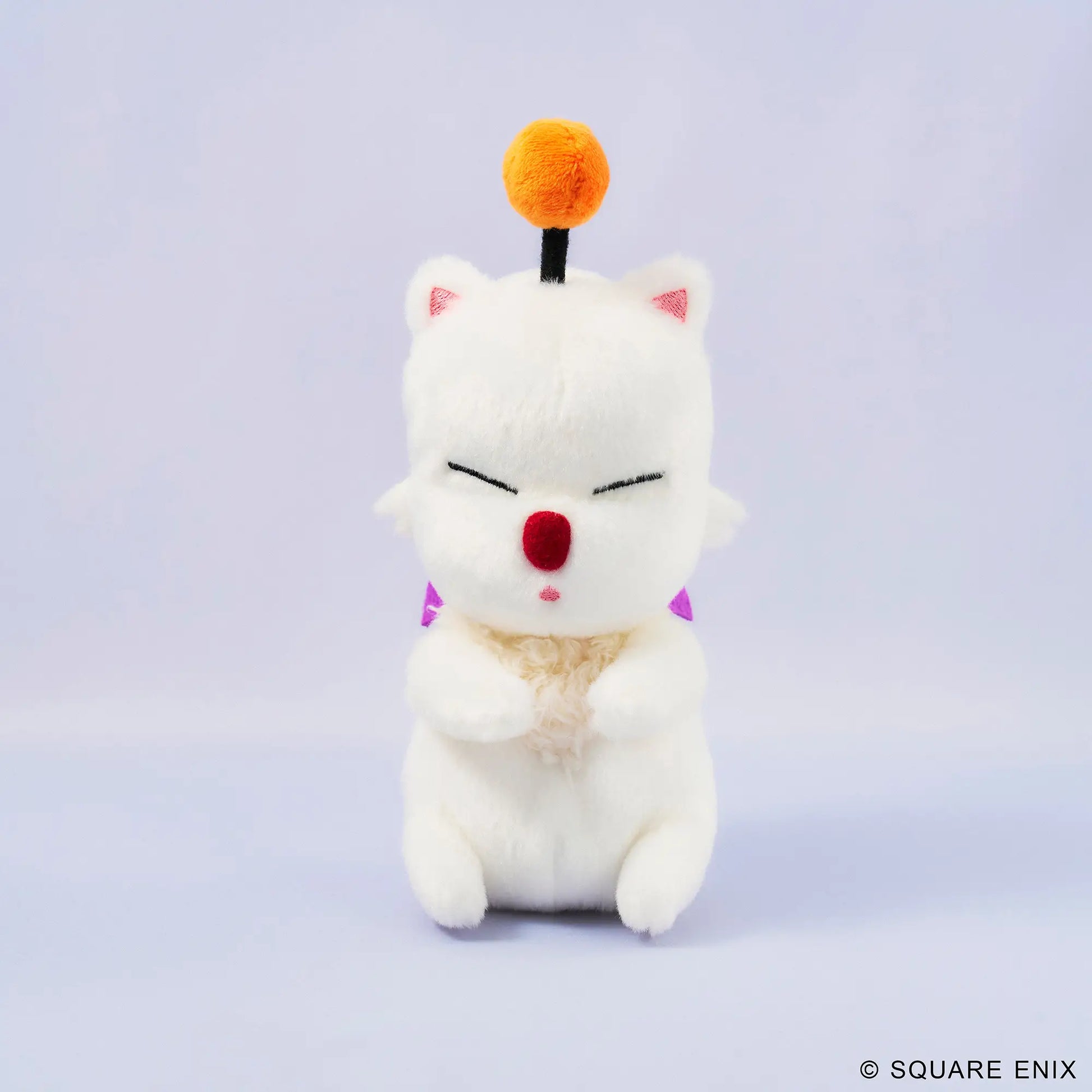 A white plush cat character toy with closed eyes, a red nose, pink inner ears, a small orange pom-pom on a black stick, and purple triangular accents, centered on a pale lavender studio background. A small Square Enix copyright mark appears in the bottom right corner.