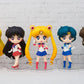 Five figurines of Sailor Moon characters on a white brick wall background