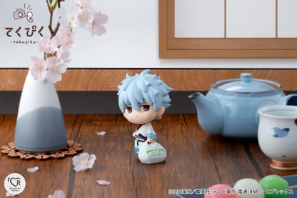 Small figurine with light blue hair next to a teapot and vase on a wooden surface.